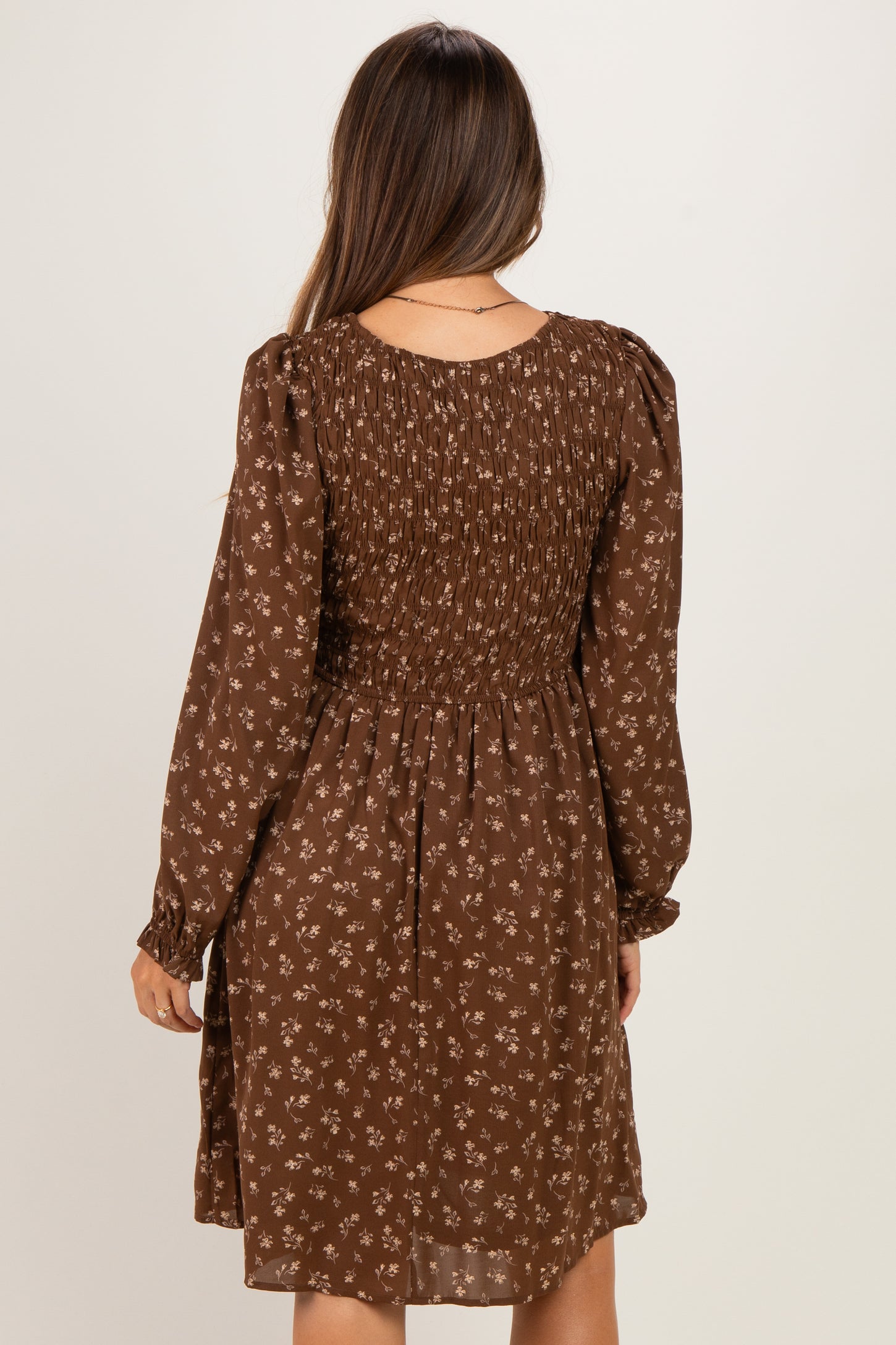 woman wearing a brown floral smocked maternity dress with long sleeves and a relaxed fit from the back