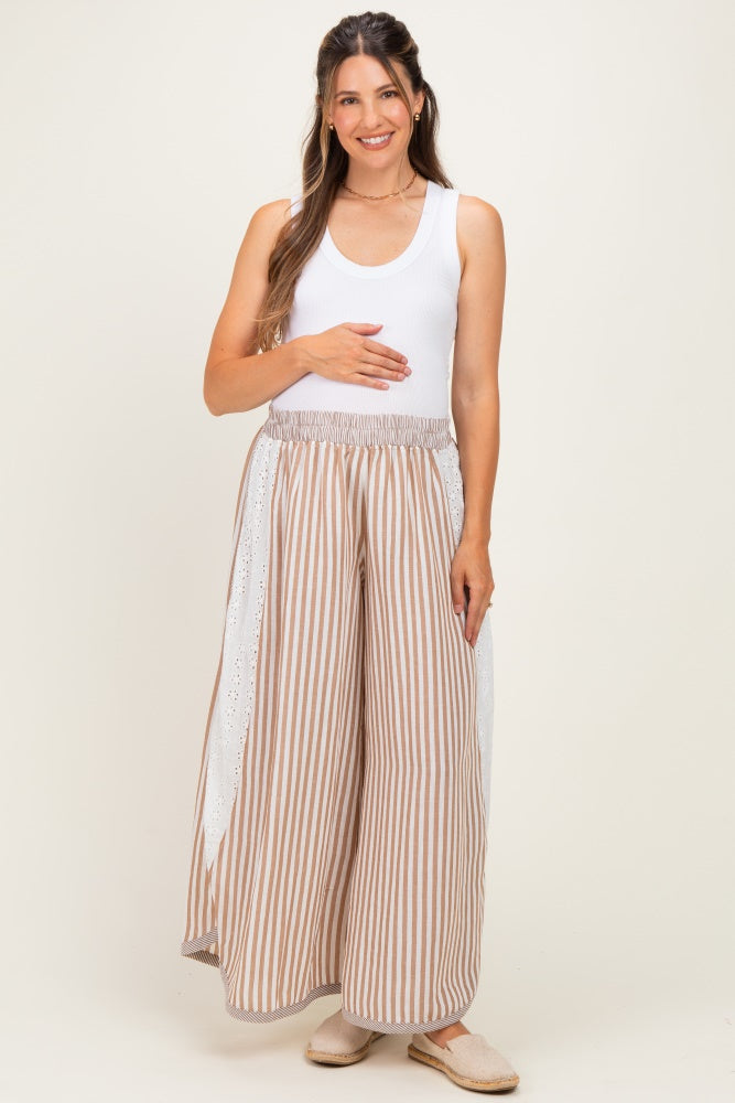 woman wearing a white tank top and striped maternity pants with eyelet detail, holding her baby bump