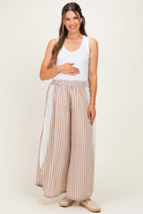 woman wearing a white tank top and striped maternity pants with eyelet detail, holding her baby bump