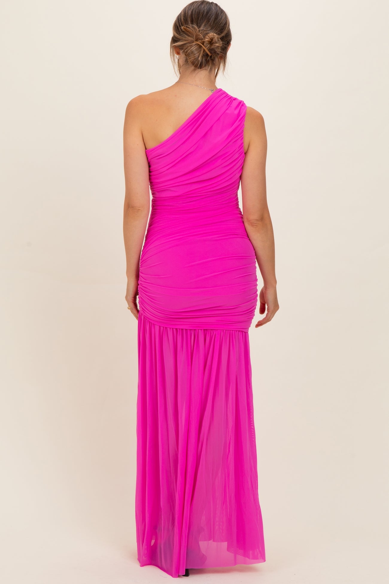 woman wearing a bright pink one-shoulder maternity gown with ruching and a flowing skirt