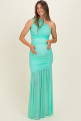 woman wearing a mint green one-shoulder maternity gown with gathered detail and a flowing skirt, holding her baby bump