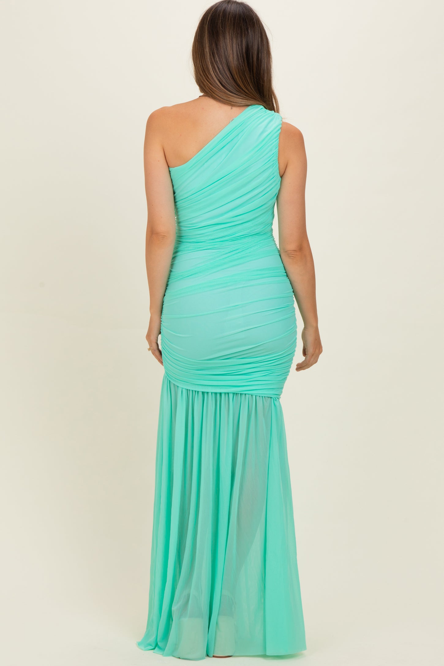 woman wearing a mint green one-shoulder maternity gown with ruched top and flowing bottom, showing a baby bump