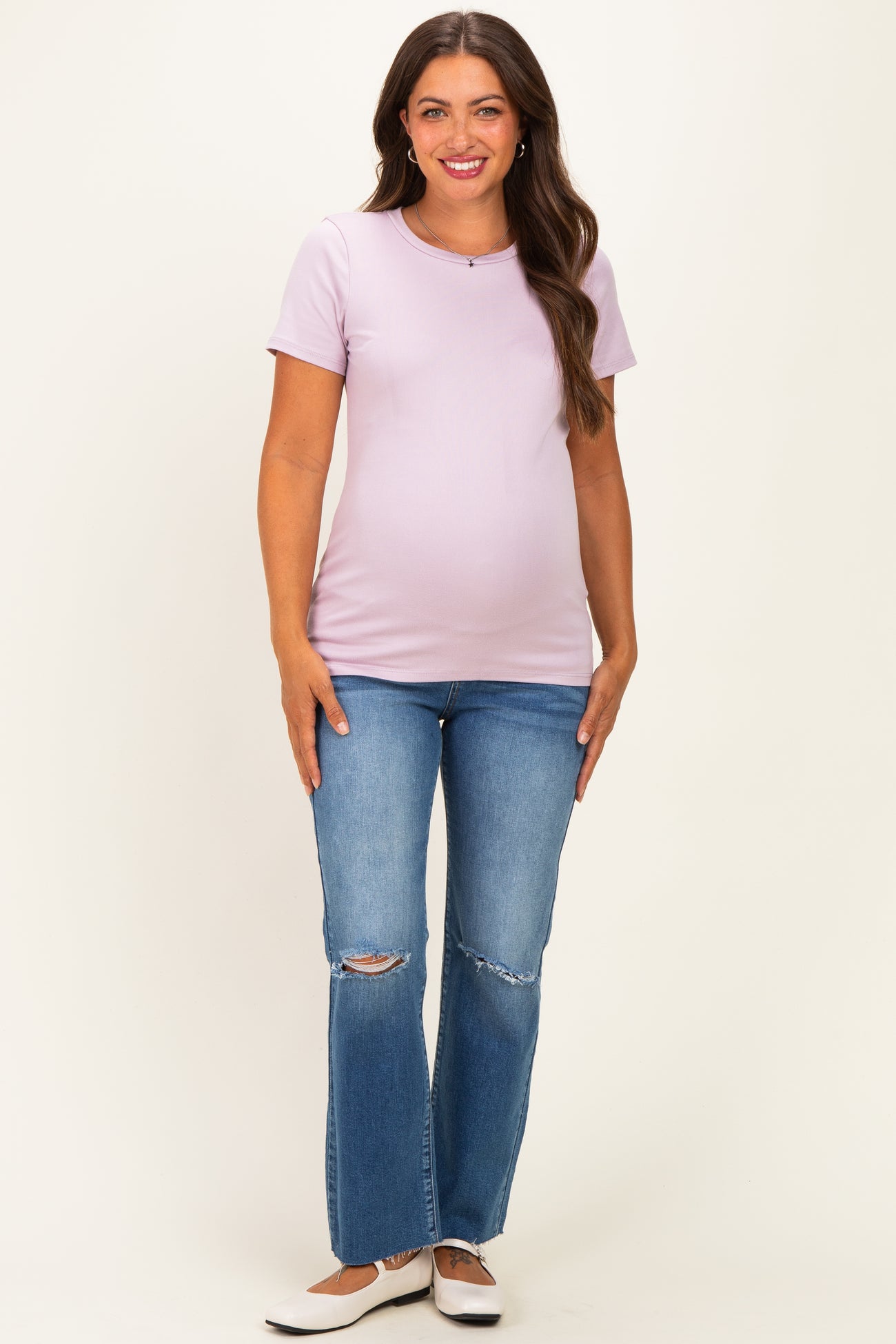 woman wearing a light purple maternity t-shirt and distressed flared jeans, showing her baby bump
