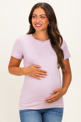 woman wearing a light purple maternity top and holding her baby bump