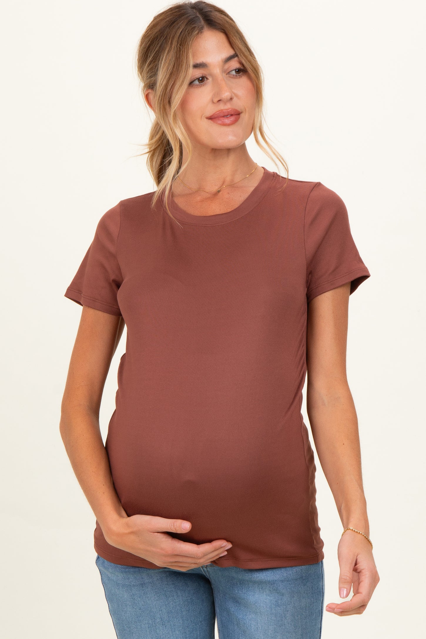 woman wearing a rust brown short sleeve maternity top and holding her baby bump