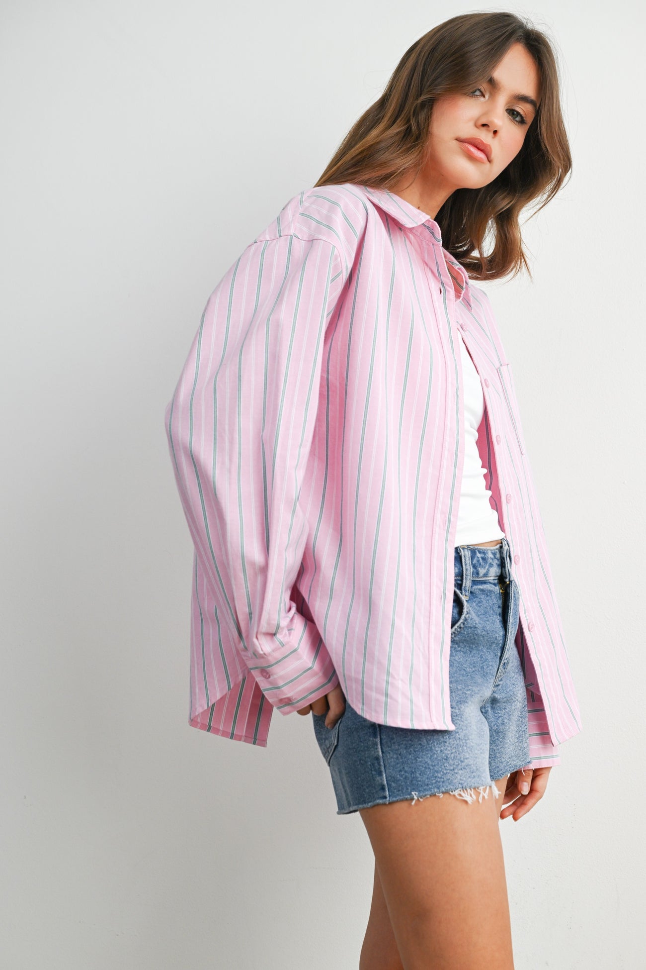 woman wearing a pink and white striped button-up shirt with long sleeves and denim shorts