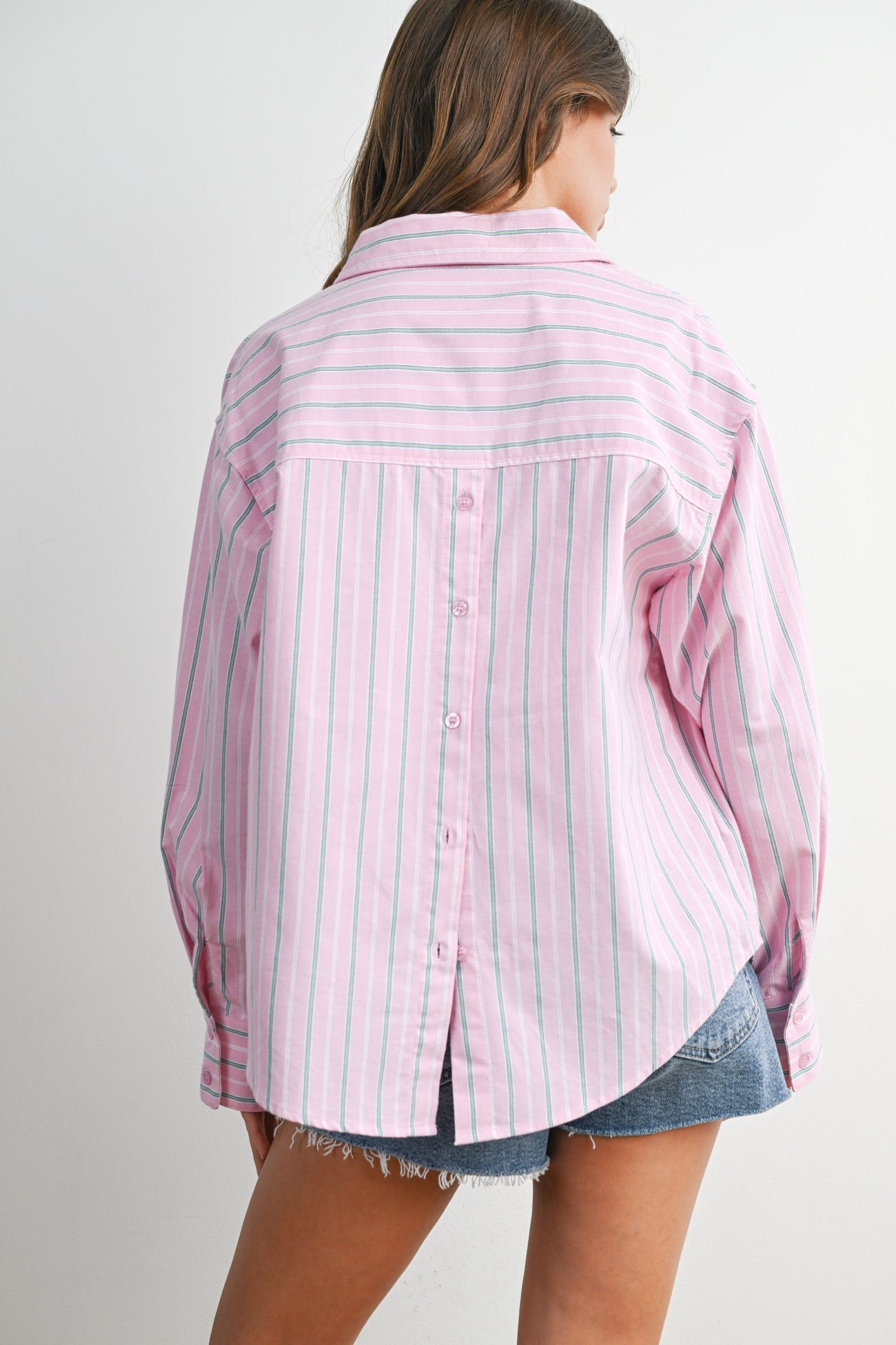 woman wearing a pink and white striped button-up shirt with a relaxed fit and rolled sleeves, paired with denim shorts
