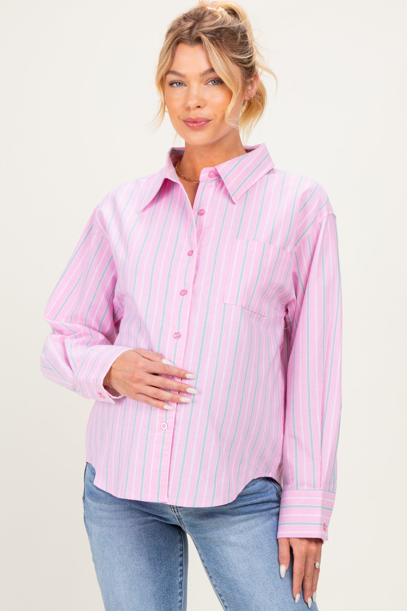 woman wearing a pink and white striped maternity shirt with buttons and a front pocket, holding her baby bump