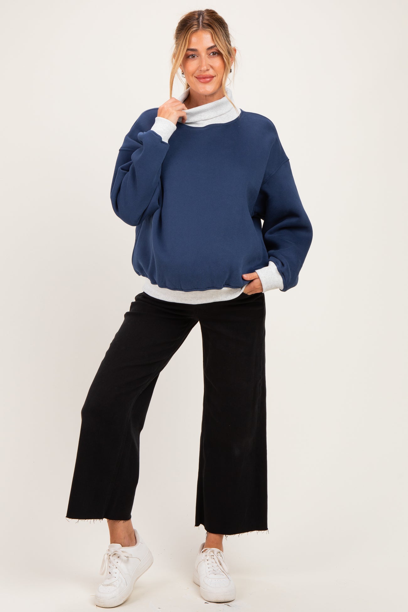 woman wearing a navy blue maternity sweatshirt with a gray turtleneck layer and black wide-leg pants