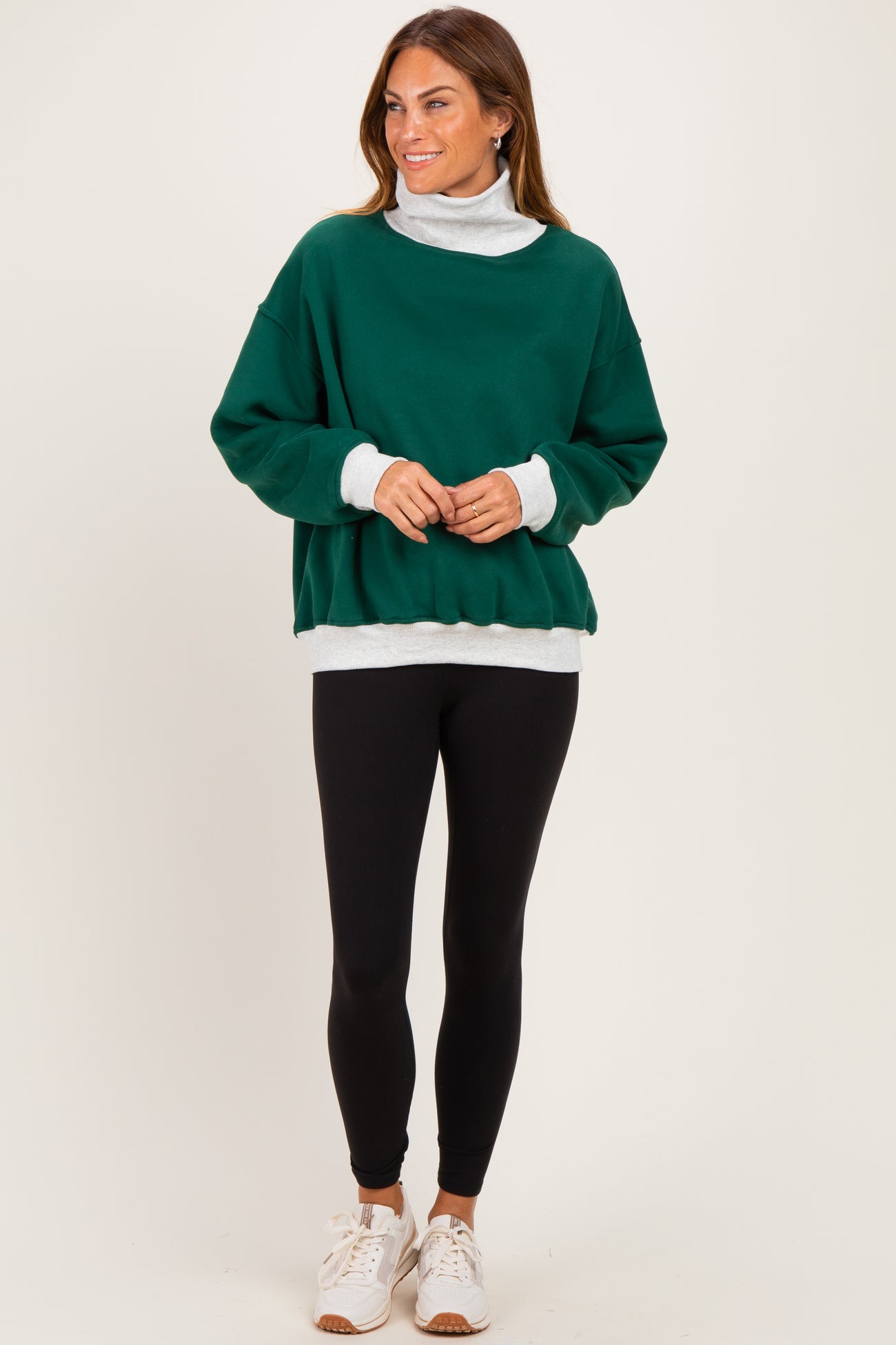 woman wearing a green oversized sweatshirt with a white turtleneck underneath, black leggings, and white sneakers