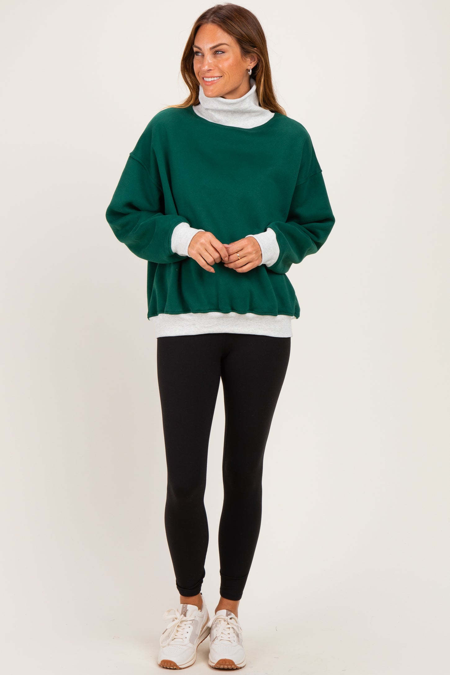 woman wearing a green oversized sweatshirt with a white turtleneck underneath, black leggings, and white sneakers