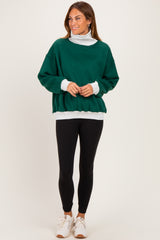 woman wearing a green oversized sweatshirt with a white turtleneck underneath, black leggings, and white sneakers