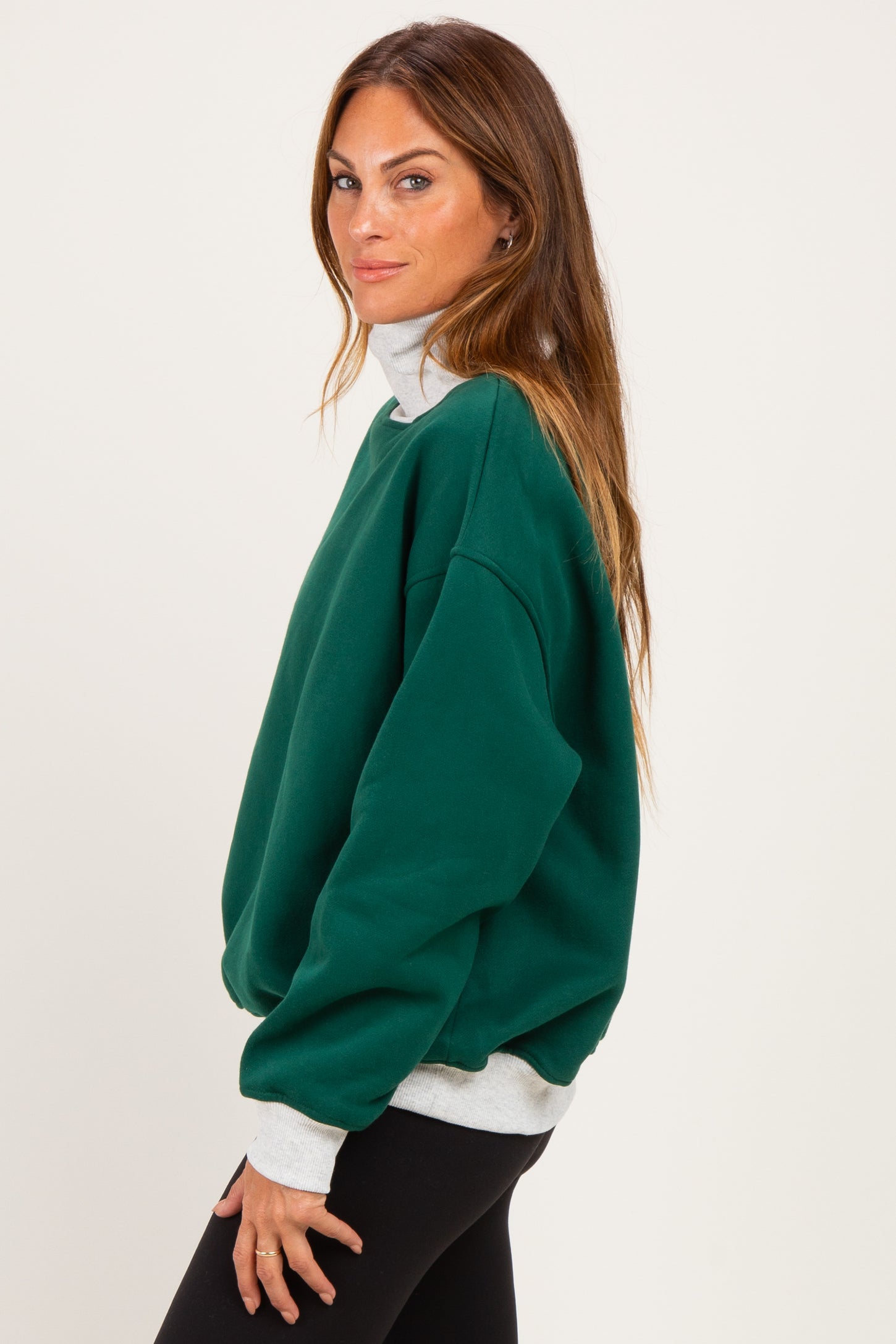 woman wearing a green oversized turtleneck sweatshirt with a light gray collar and black leggings