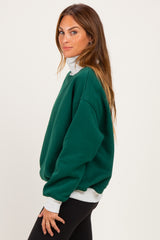 woman wearing a green oversized turtleneck sweatshirt with a light gray collar and black leggings