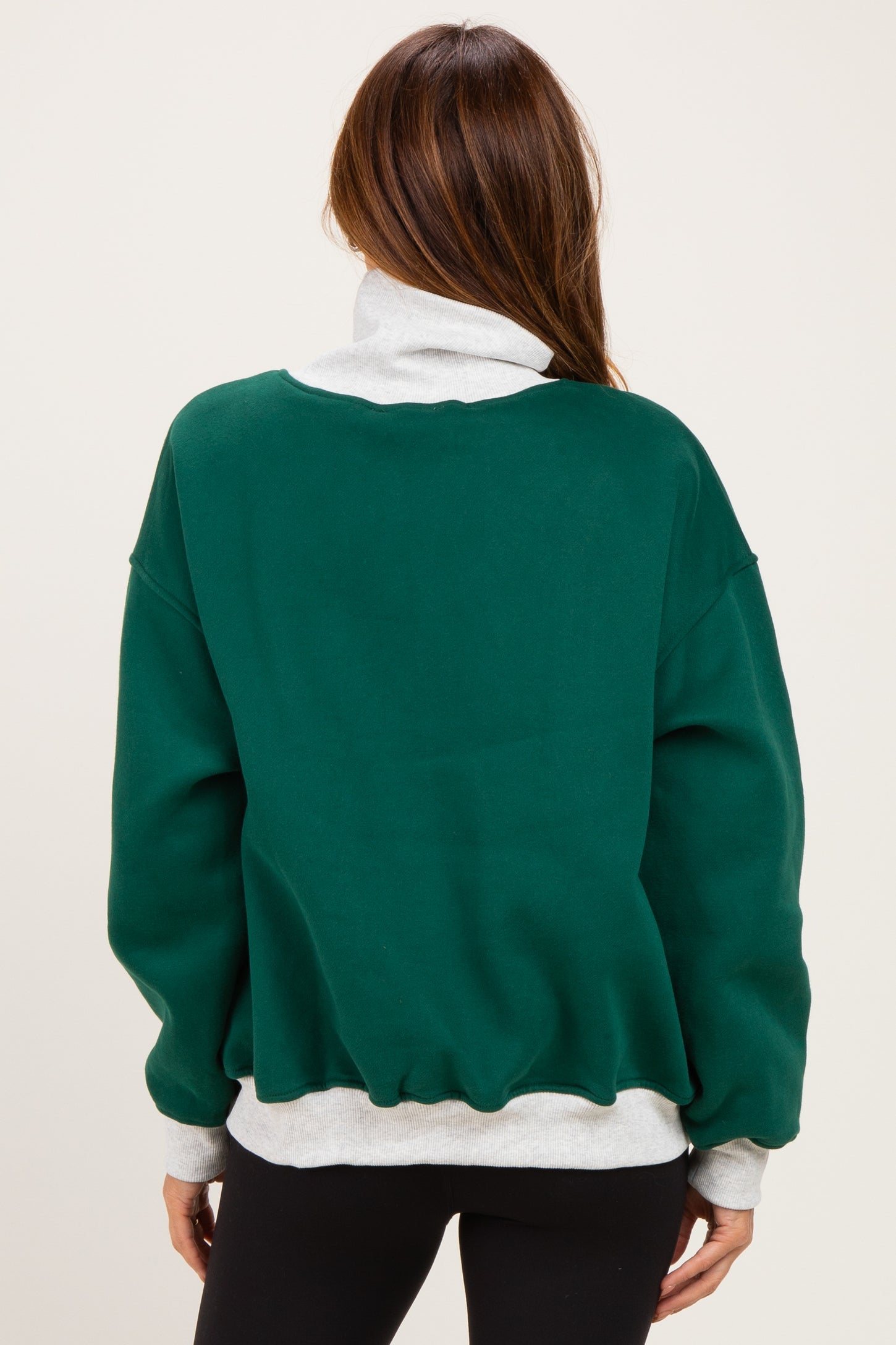 woman wearing a green oversized sweatshirt with a white collar and hem, shown from the back