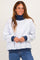 woman wearing a light grey oversized sweatshirt with a navy turtleneck and navy cuffs, smiling against a neutral background