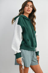 woman wearing a green and gray color block hoodie styled with plaid shorts
