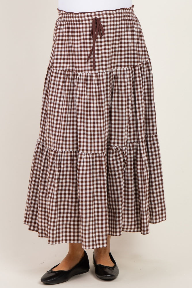 woman wearing a brown and white gingham patterned maternity maxi skirt with a drawstring waist and tiered design