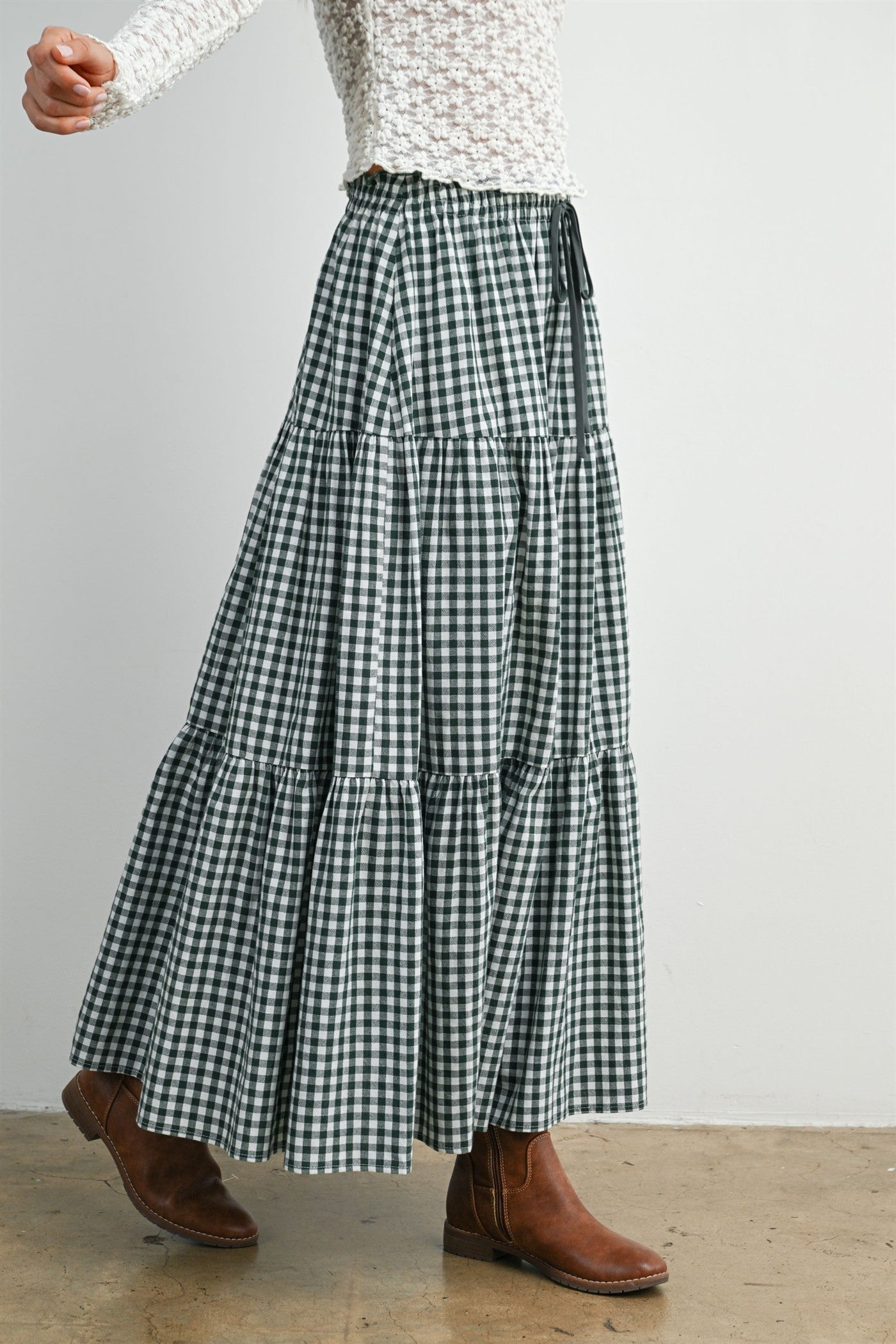 woman wearing a green and white gingham tiered maxi skirt paired with brown ankle boots