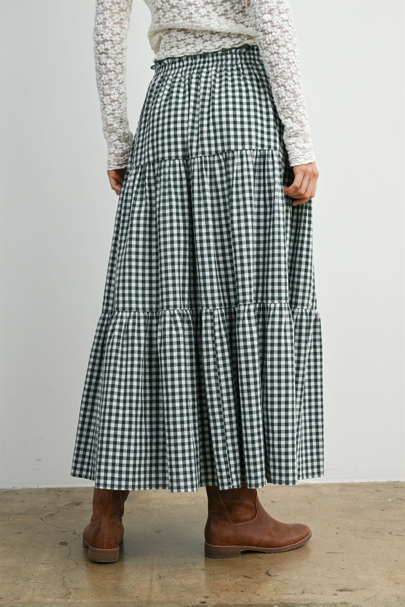 woman wearing a green and white gingham maxi skirt with tiered ruffles, styled with brown ankle boots