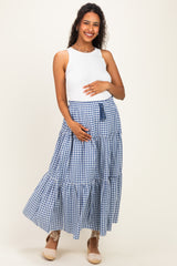 woman wearing a white sleeveless maternity top and a blue gingham tiered maxi skirt, holding her baby bump