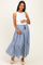woman wearing a white sleeveless maternity top and a blue gingham tiered maxi skirt, holding her baby bump