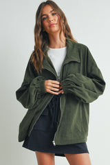 woman wearing an olive green corduroy jacket with a zip front and puffed sleeves, paired with a white top and black shorts