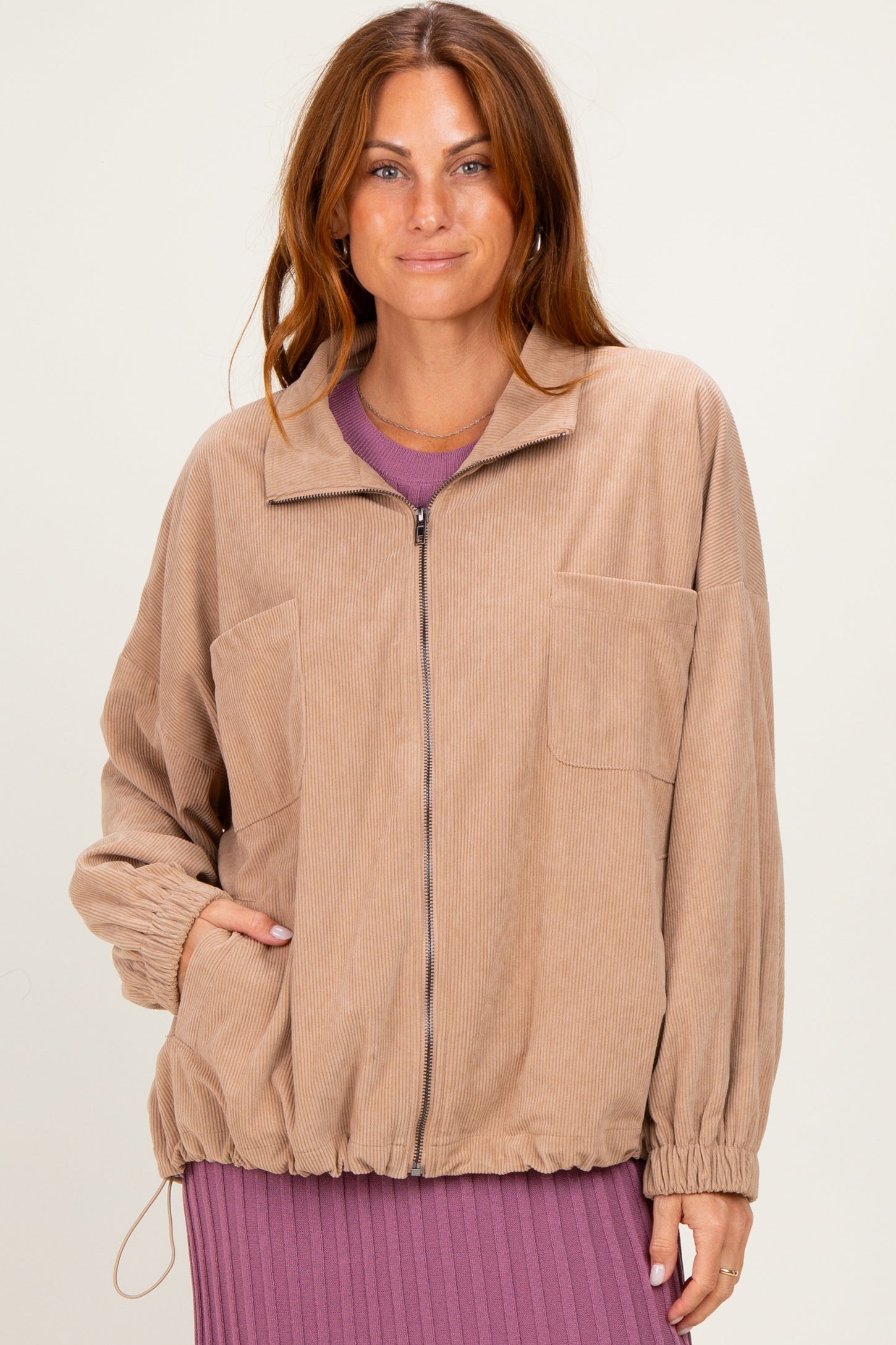 woman wearing a light brown corduroy zip-up jacket with two front pockets and elasticized hem over a purple dress