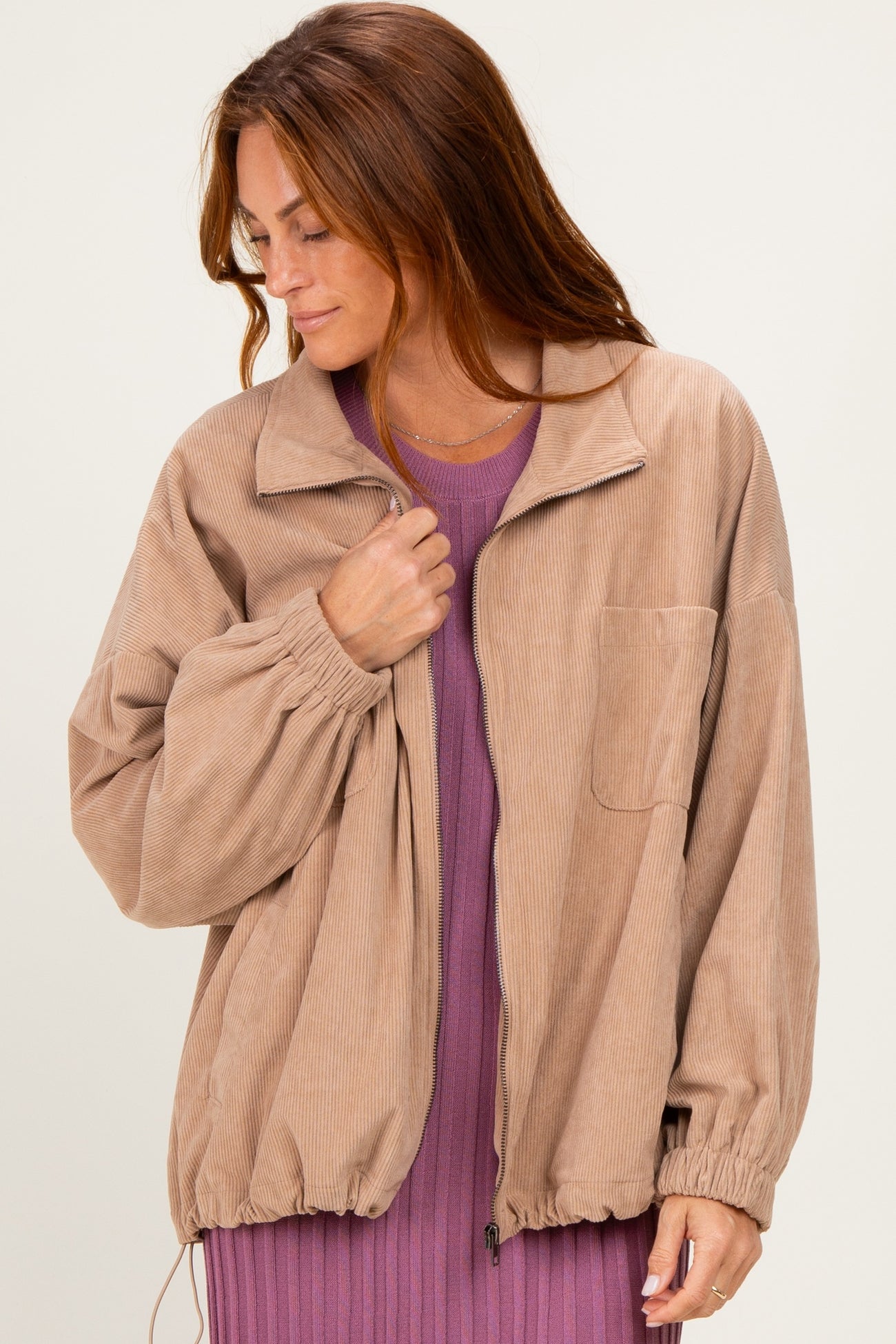 woman wearing a tan corduroy jacket with a zip front and oversized fit over a purple ribbed dress