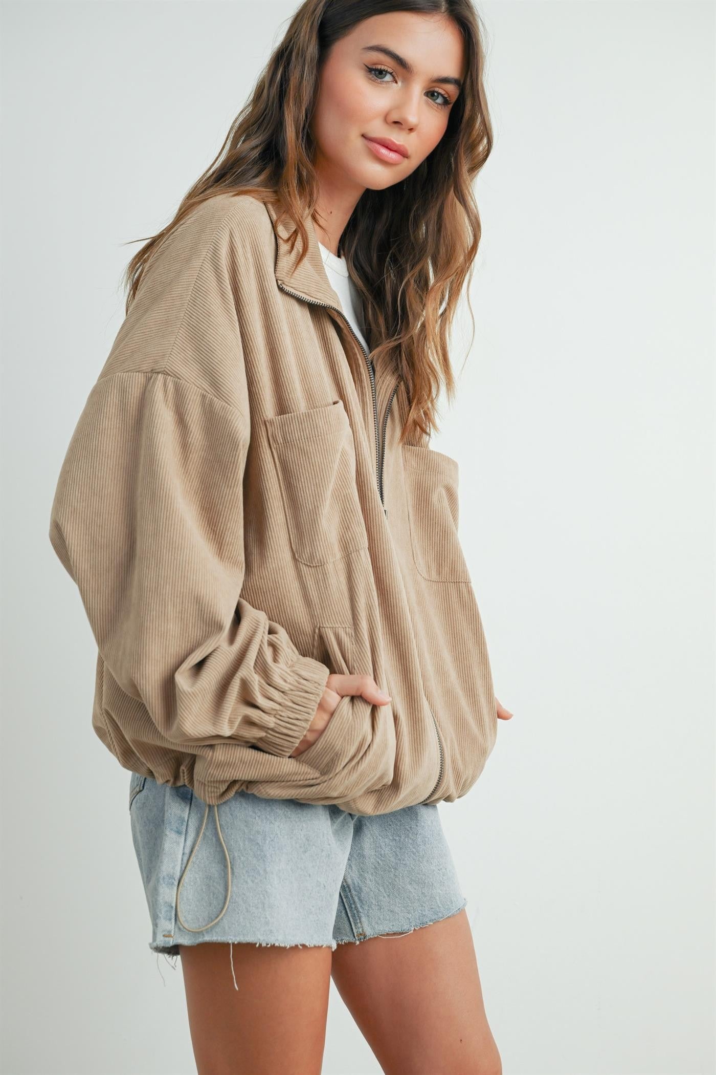 woman wearing a beige corduroy zip-up jacket with two front pockets and light denim shorts