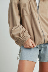 woman wearing a tan corduroy zip-up jacket with puffed sleeves and denim shorts