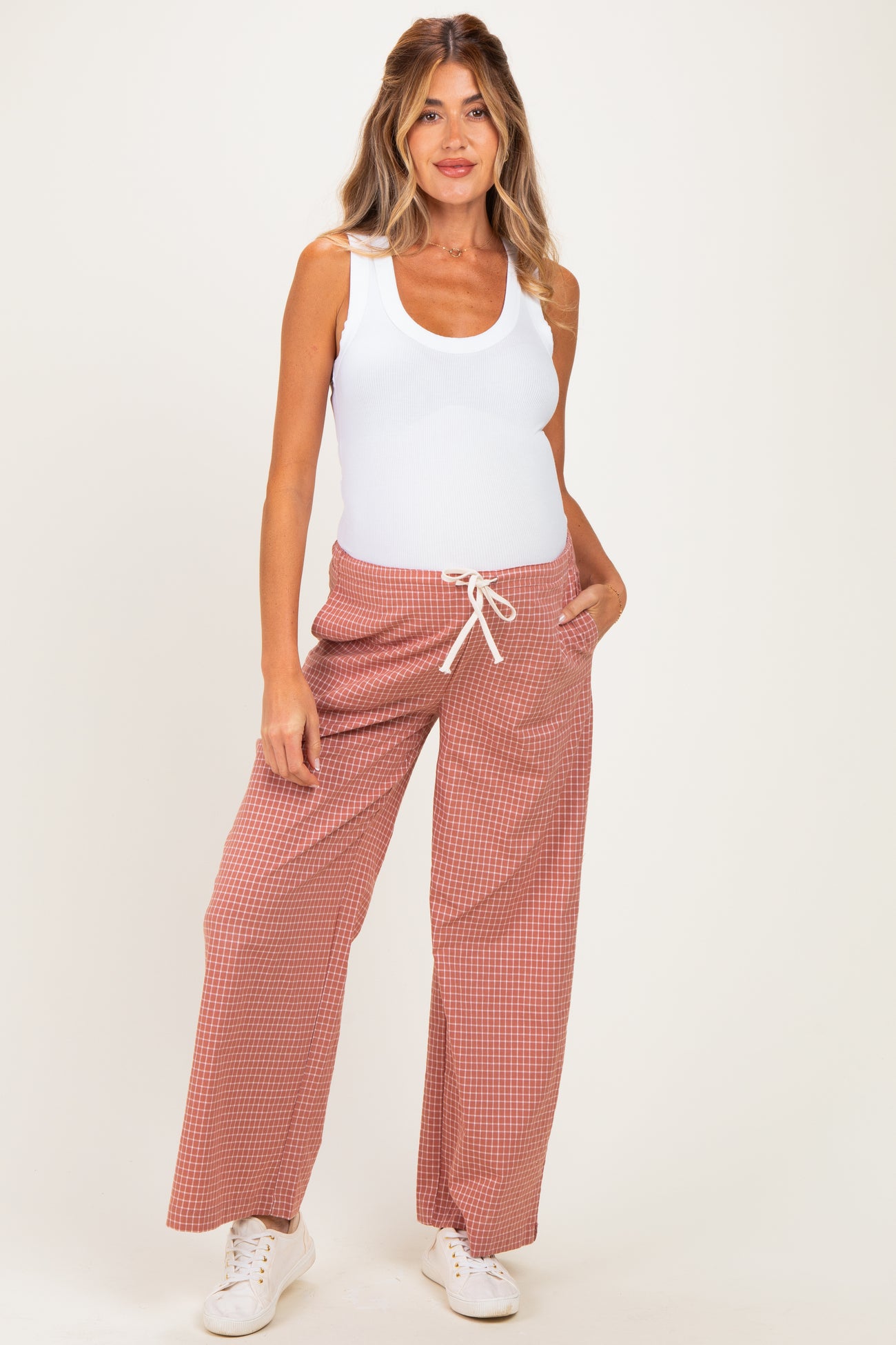 woman wearing a white tank top and red checkered maternity pants with a side pocket and drawstring waist, showing baby bump