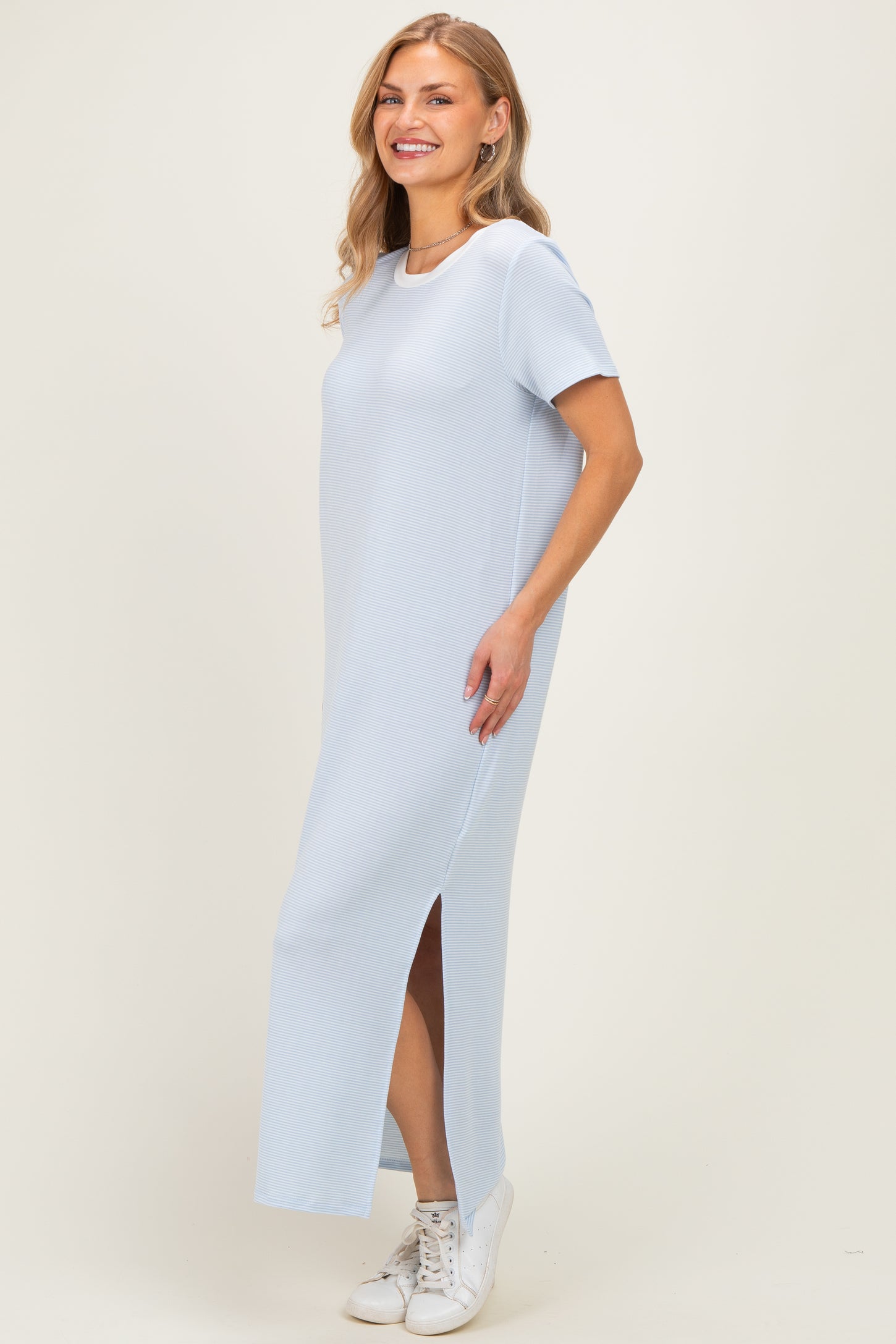 woman wearing a light blue maxi dress with short sleeves and side slits, paired with white sneakers