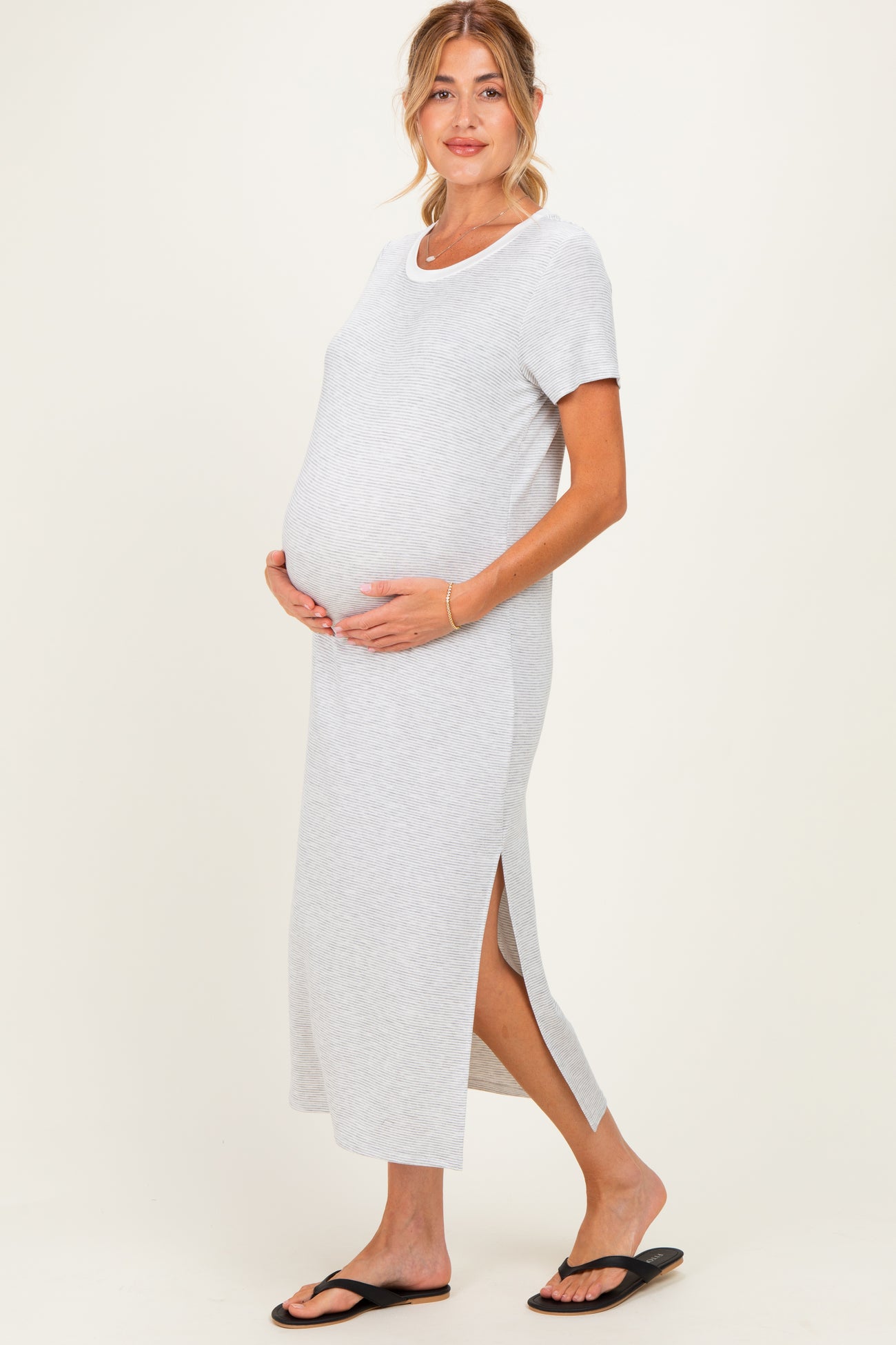 woman wearing a gray maternity maxi dress with short sleeves and side slits, showcasing her baby bump