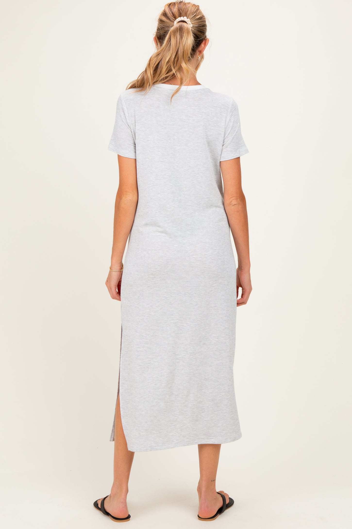 woman wearing a gray short sleeve maxi maternity dress with a side slit, viewed from the back