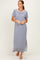 woman wearing a gray maxi dress with short sleeves and a white neckline, standing against a light background