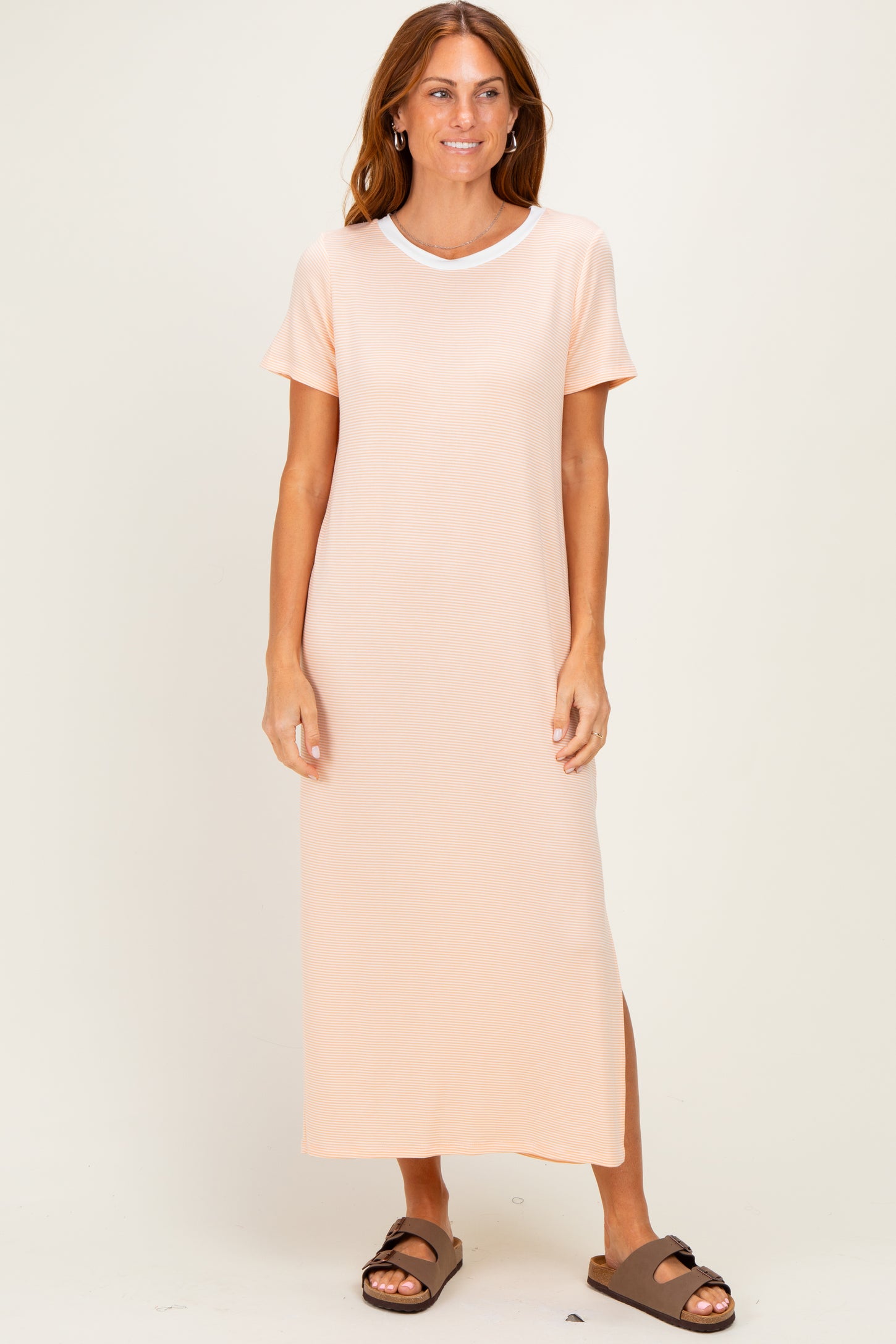 woman wearing a light peach short sleeve maxi dress with a round neckline and side slit, standing and smiling