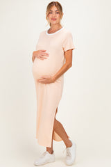 woman wearing a light peach maternity maxi dress with short sleeves and a side slit, holding her baby bump