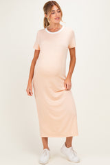 woman wearing a light peach short sleeve maternity dress with a relaxed fit and side pockets, holding her baby bump