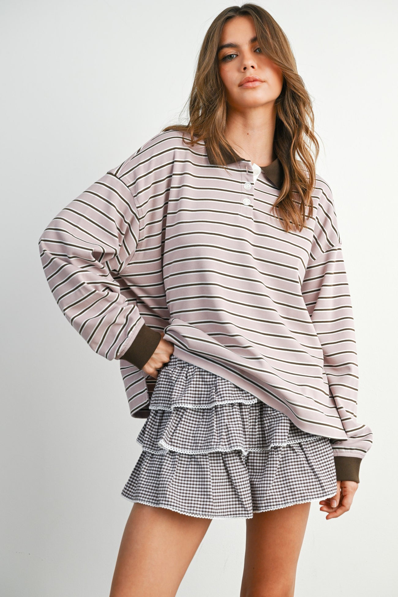 woman wearing a light pink and brown striped oversized sweatshirt and a black and white gingham ruffled skirt