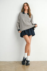 woman wearing a striped oversized polo sweater with a navy collar and denim shorts, paired with white socks and sneakers