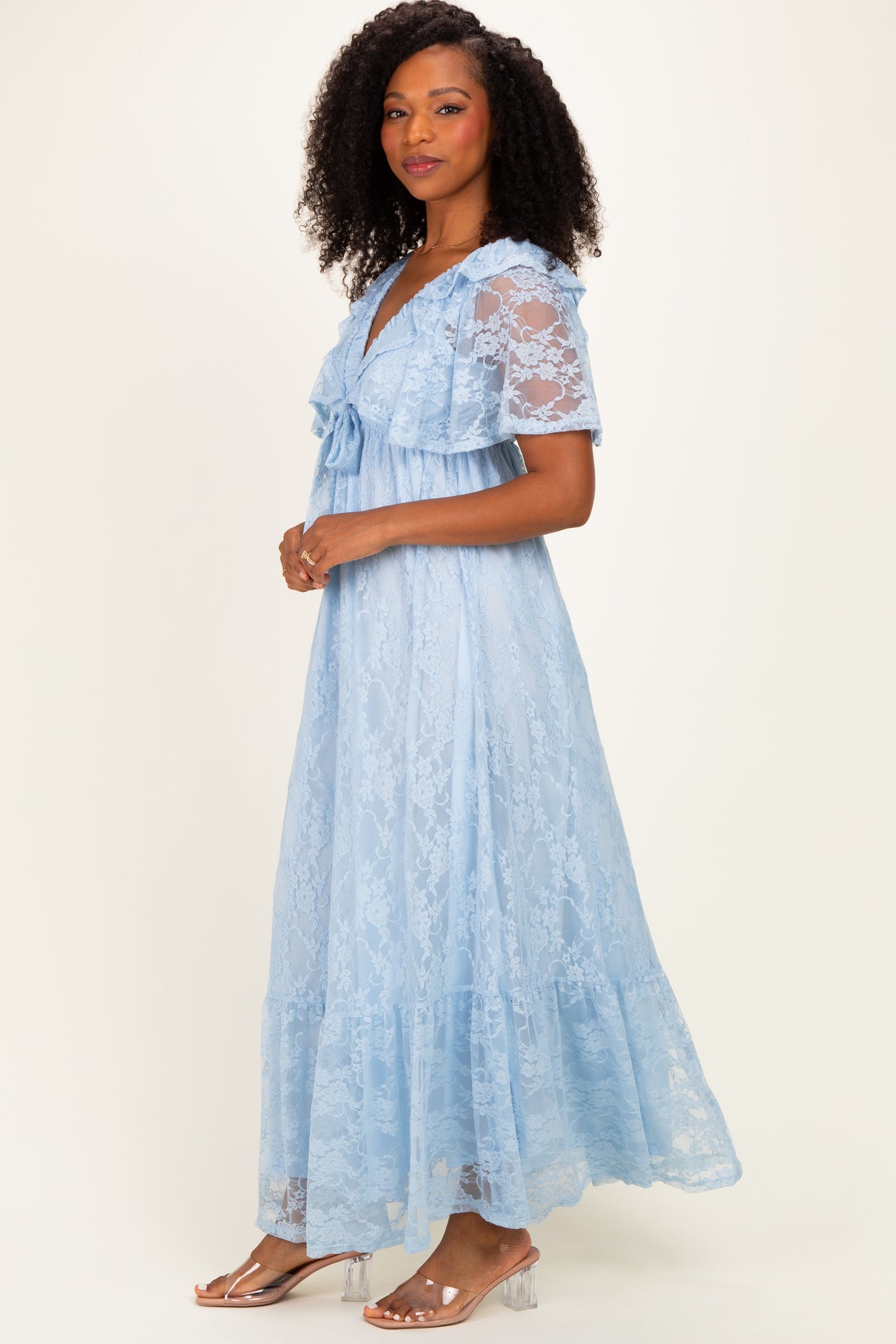 woman wearing a light blue lace maxi dress with short sleeves and a ruffled hem, posed sideways against a neutral background