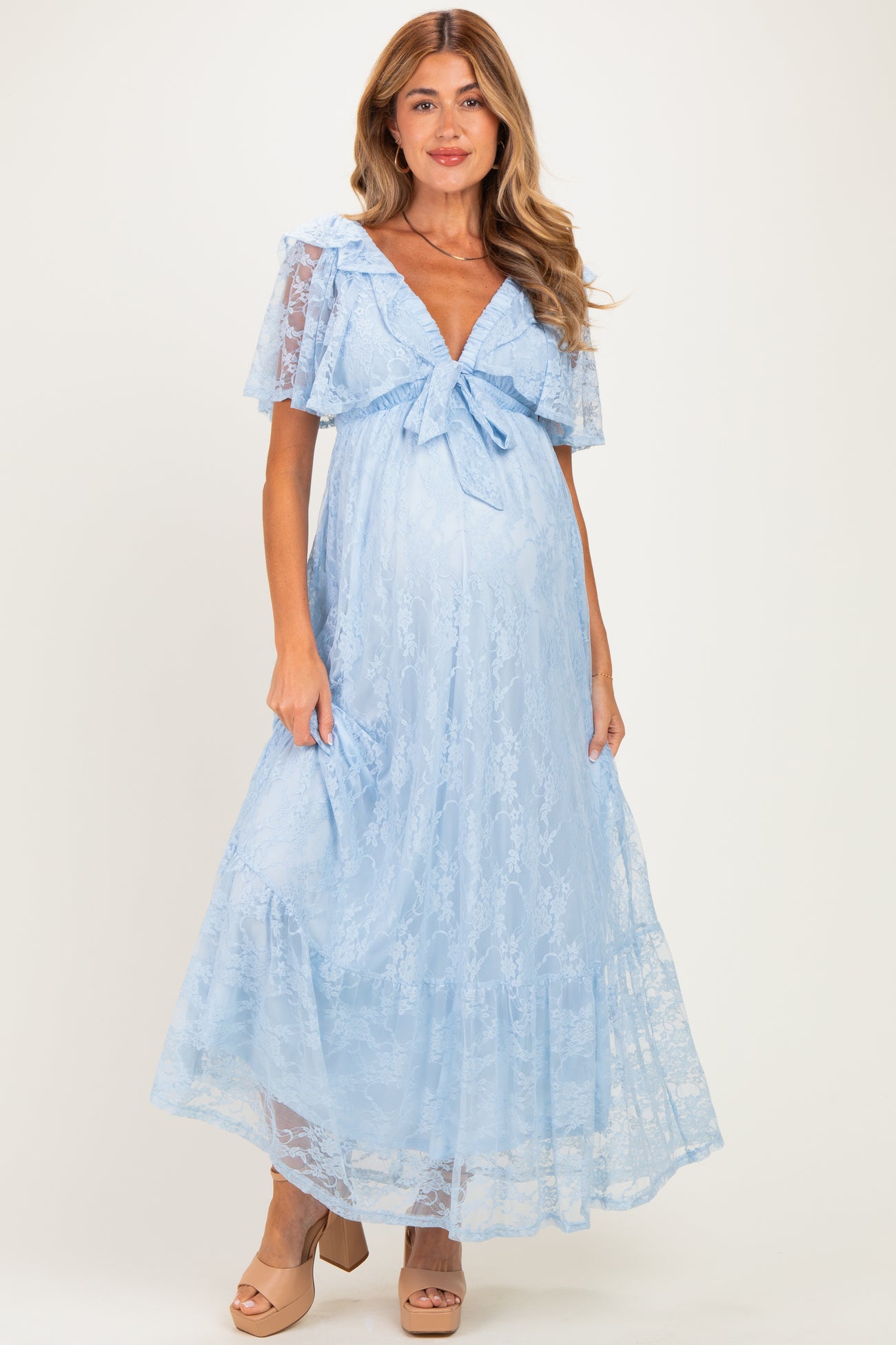 woman wearing a light blue lace maternity maxi dress with a bow detail and short flutter sleeves, showcasing her baby bump