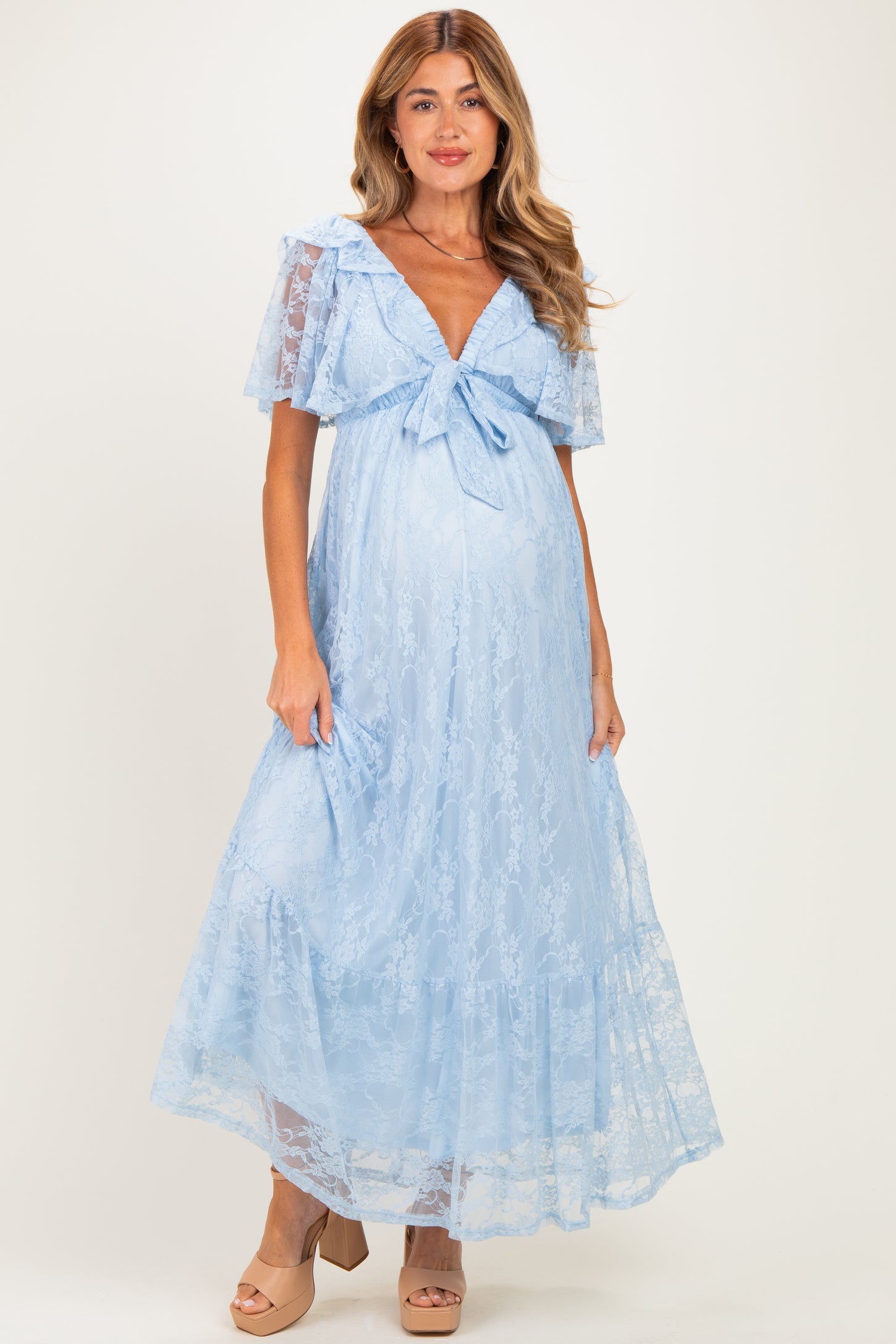 woman wearing a light blue lace maternity maxi dress with a bow detail and short flutter sleeves, showcasing her baby bump