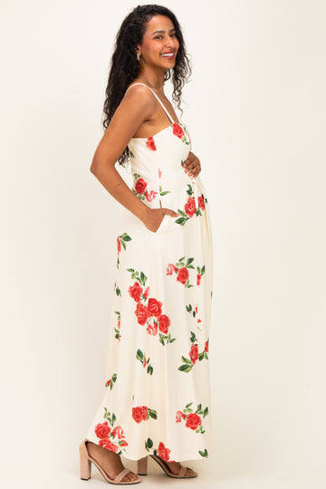 woman wearing a cream floral maternity maxi dress with a baby bump and pockets, smiling and standing sideways