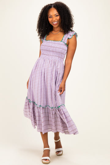 woman wearing a purple checkered sundress with gathered bodice and ruffled sleeves, standing and smiling