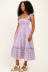 woman wearing a lilac plaid midi dress with smocked bodice and ruffled sleeves, paired with wedge sandals