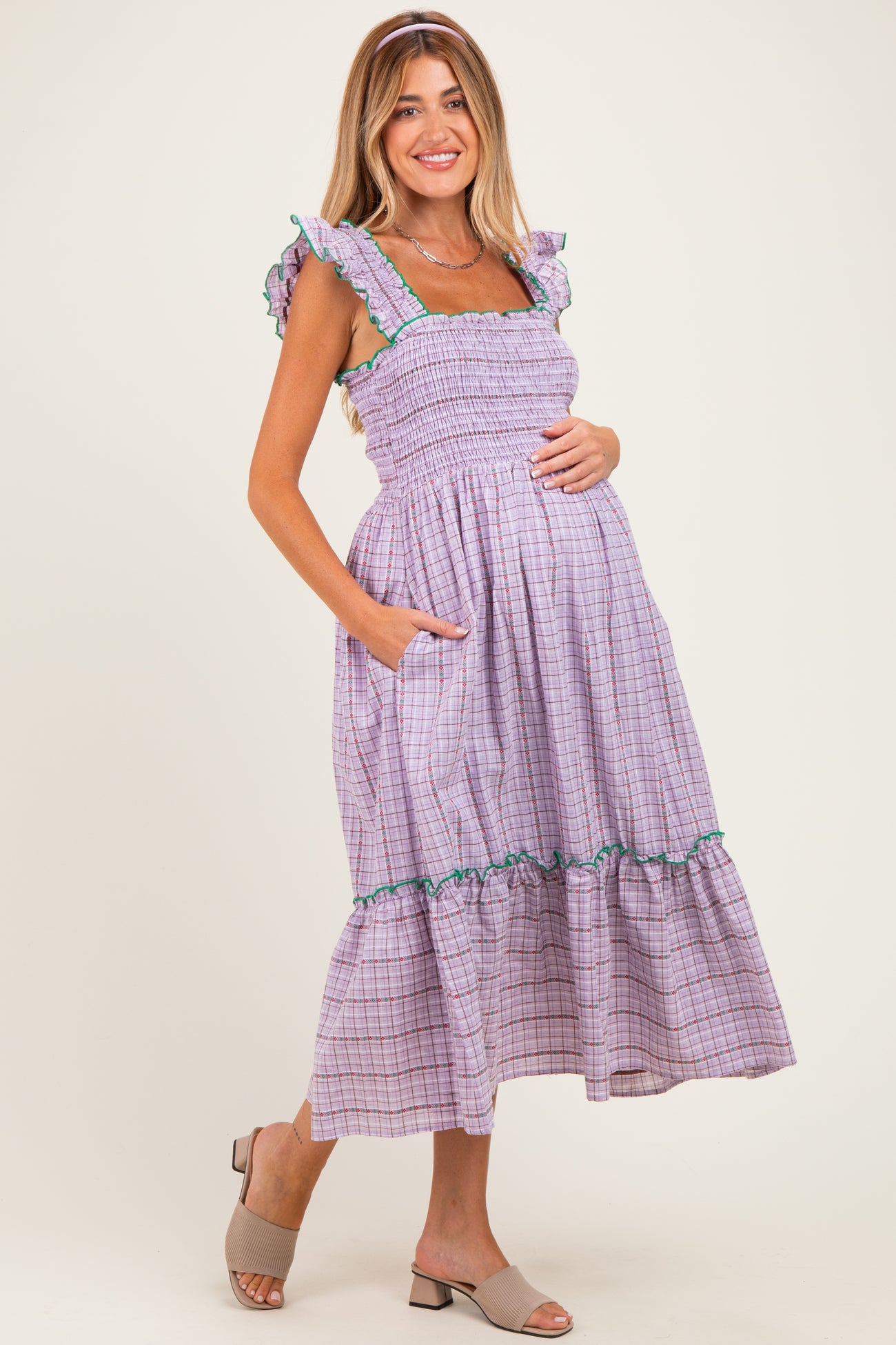 woman wearing a lavender and white checkered maternity dress with ruffled straps and pockets, showcasing her baby bump