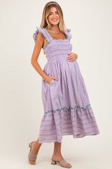 woman wearing a lavender and white checkered maternity dress with ruffled straps and pockets, showcasing her baby bump