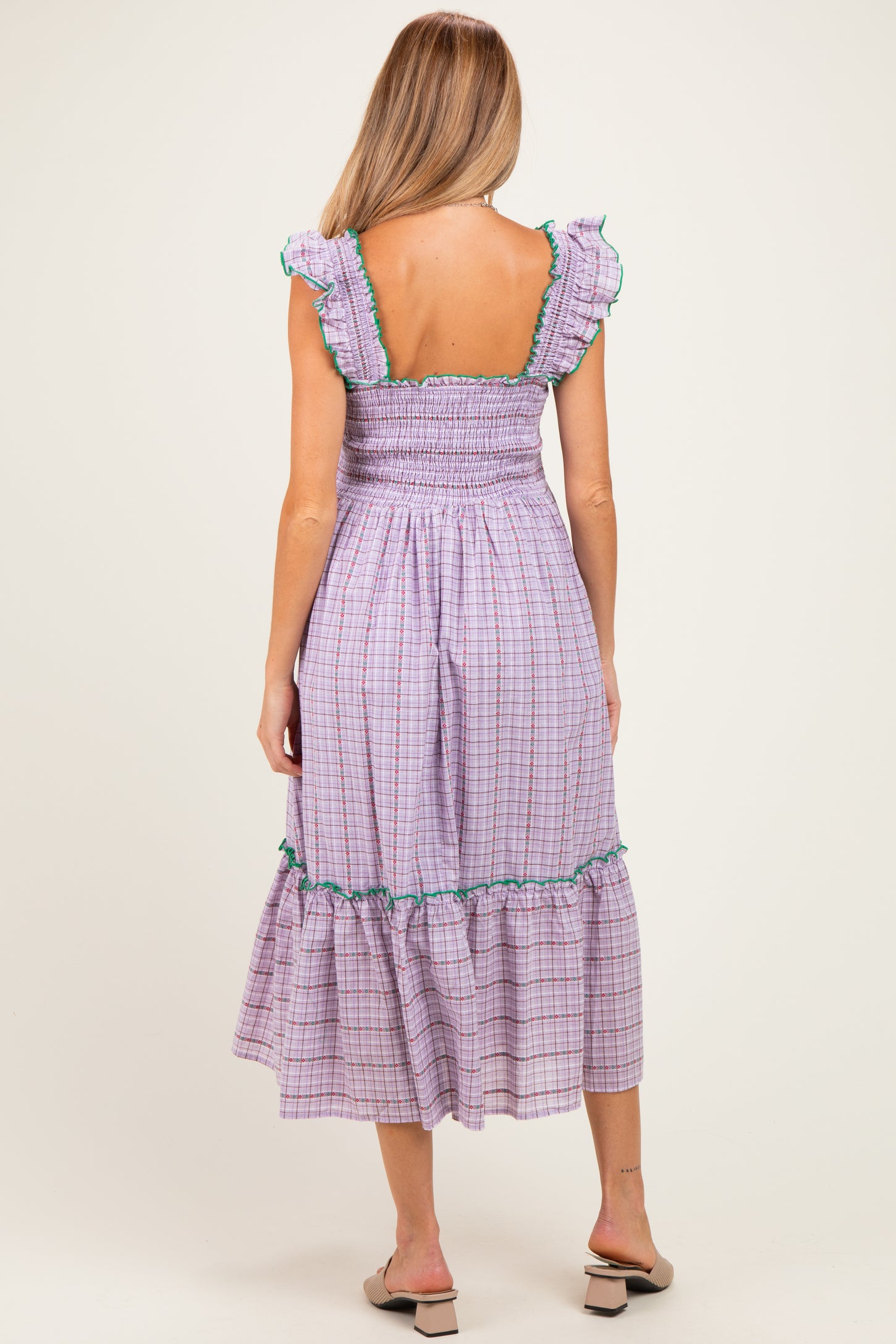 woman wearing a purple and green checkered maternity dress with ruffled sleeves and a tiered skirt, showing her back